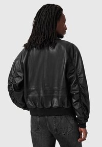 Czarna skórzana kurtka bomberka z marszczonymi rękawami, ściągaczami na mankietach i u dołu. Charakteryzuje się gładką fakturą i czystymi liniami designu w krótkim kroju.