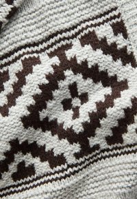 Strikket stof med et geometrisk mønster i mørkebrun og creme, med en struktureret overflade og et stribet bånd langs kanten.