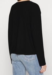 Schwarzes, geripptes Langarmoberteil mit seitlichen Schlitzen, weitem Ausschnitt und lockerer Passform, kombiniert mit hellblauen Jeans.