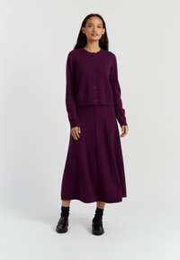 Cardigan lavorato a maglia viola con scollatura rotonda e bottoni, abbinato a una lunga gonna coordinata. Tessuto morbido, materiale caldo e design a strati.