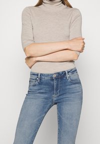 Top beige de manga corta con cuello alto, combinado con unos jeans de denim azul claro, que presentan un clásico diseño de cinco bolsillos y un ligero desgaste.