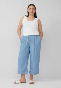 Top sans manches blanc associé à un pantalon court léger bleu clair, ample, avec une taille élastique et un cordon de serrage agrémenté de perles en bois.