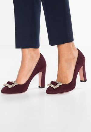 Escarpins en daim bordeaux avec un nœud bijou orné à l'avant. Dotés d'un talon empilé transparent et d'une texture lisse et mate.