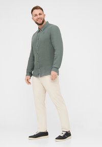 Camicia verde con bottoni, realizzata in tessuto leggero, abbinata a pantaloni color crema e sneakers nere. Caratterizzata da una vestibilità rilassata e orlo arrotondato.