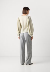 Lichtgroene blouse met textuur en pofmouwen, gecombineerd met grijze pinstriped broek. De outfit heeft een vierkante halsopening aan de achterkant.