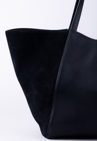 Black tote bag featuring a combination of smooth leather and suede texture. Designed with a triangular shape and reinforced seams.