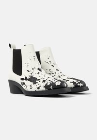 Botas de tobillo blancas de cuero con un patrón de salpicaduras negras y paneles laterales elásticos, punta redonda y un bajo tacón negro. Acabado texturizado.
