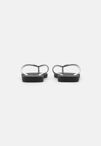 Sorte flip-flopper med flat såle og hvite detaljer. Remmene er laget av gummi, og danner et enkelt, åpent design uten utsmykkinger.