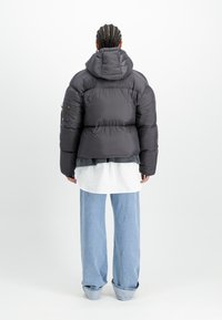 Zwarte gewatteerde jas met capuchon, lange mouwen en een cropped ontwerp. Gekenmerkt over een witte shirt en gecombineerd met lichtblauwe wijde spijkerbroeken.