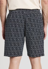 Pantaloni corti neri con un motivo geometrico bianco, vita elasticizzata, design fino al ginocchio e dettagli in tessuto testurizzato.