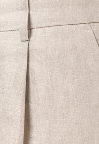 Gros plan sur un tissu en lin beige avec une taille, une passants de ceinture et un détail de pli sur un vêtement.