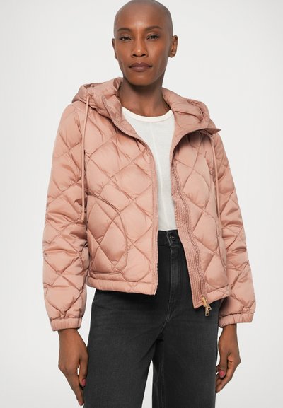 Giacca trapuntata rosa chiaro con cappuccio, caratterizzata da cuciture diagonali, chiusura con zip e polsini elasticizzati. Indossata sopra una maglietta bianca e jeans scuri.