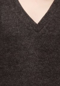Gros plan d'un pull en laine texturé brun foncé avec un col en V sur une peau claire.
