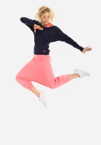 Granatowa bluza z luźnym krojem i różowe dresy z elastycznymi mankietami, zestawione z białymi sneakersami. Temat skacze na białym tle.