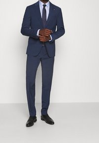 Námořnický oblek s přiléhavým střihem, texturovaná tkanina a jednobodový blejzr. Doplněno světle modrou košilí a vzorovanou kravatou. Černé boty.