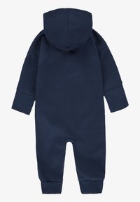 Tengerészkék pamut overall kapucnival, hosszú ujjakkal, bordázott mandzsettákkal és láb nélküli kialakítással. Simogató tapintású, minimalista stílusú, patent nélküli.