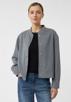 Gray jacket made of soft, textured fabric; snap-button closure; cropped design; rounded neckline; worn over a black top and blue jeans.