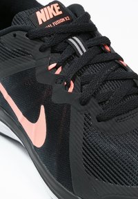 Black Nike Fusion X2 sneaker with pink accents, textured mesh upper, and black laces. Features a white outsole and branding on the tongue.