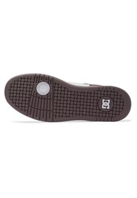 DC Shoes sneaker sole with a textured, brown rubber outsole. Features a circular logo and a grid pattern for grip.