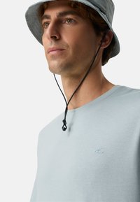 Lichtblauw katoenen T-shirt met een ronde hals en korte mouwen, voorzien van een klein logo op de linkerborst. Grijze bucket hat met een kinriem.