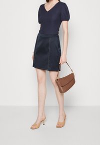 Námořnická tričko s krátkým rukávem s texturovaným vzorem, spárované s námořnickou saténovou sukní s kontrastním šitím. Doplňky zahrnují hnědou kabelku a tělové podpatky.