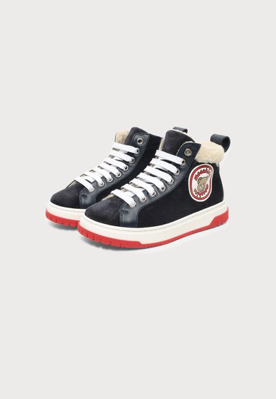 Baskets montantes noires avec des lacets blancs, des semelles rouges, une doublure en fourrure et un patch rond présentant un logo d’ours sur le côté.