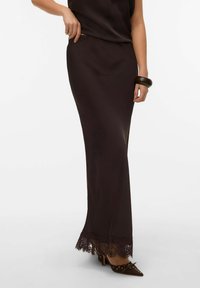 Pitkä musta hame, joka on valmistettu sileästä kankaasta ja jossa on pitsinen helmikoriste. Suora siluetti ja hienovarainen kiilto. Yhdistetty kärkipäisiin korkokenkiin.