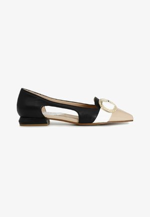 Chaussure plate en cuir noir, blanc et beige avec un bout pointu, des côtés découpés et un accent circulaire décoratif sur le devant. Talon bas et carré.