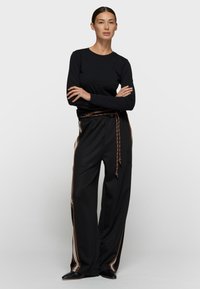 Top negro de manga larga combinado con pantalones negros sueltos que presentan un acento de rayas marrones y cinturón a juego, todo en un material suave y liso.