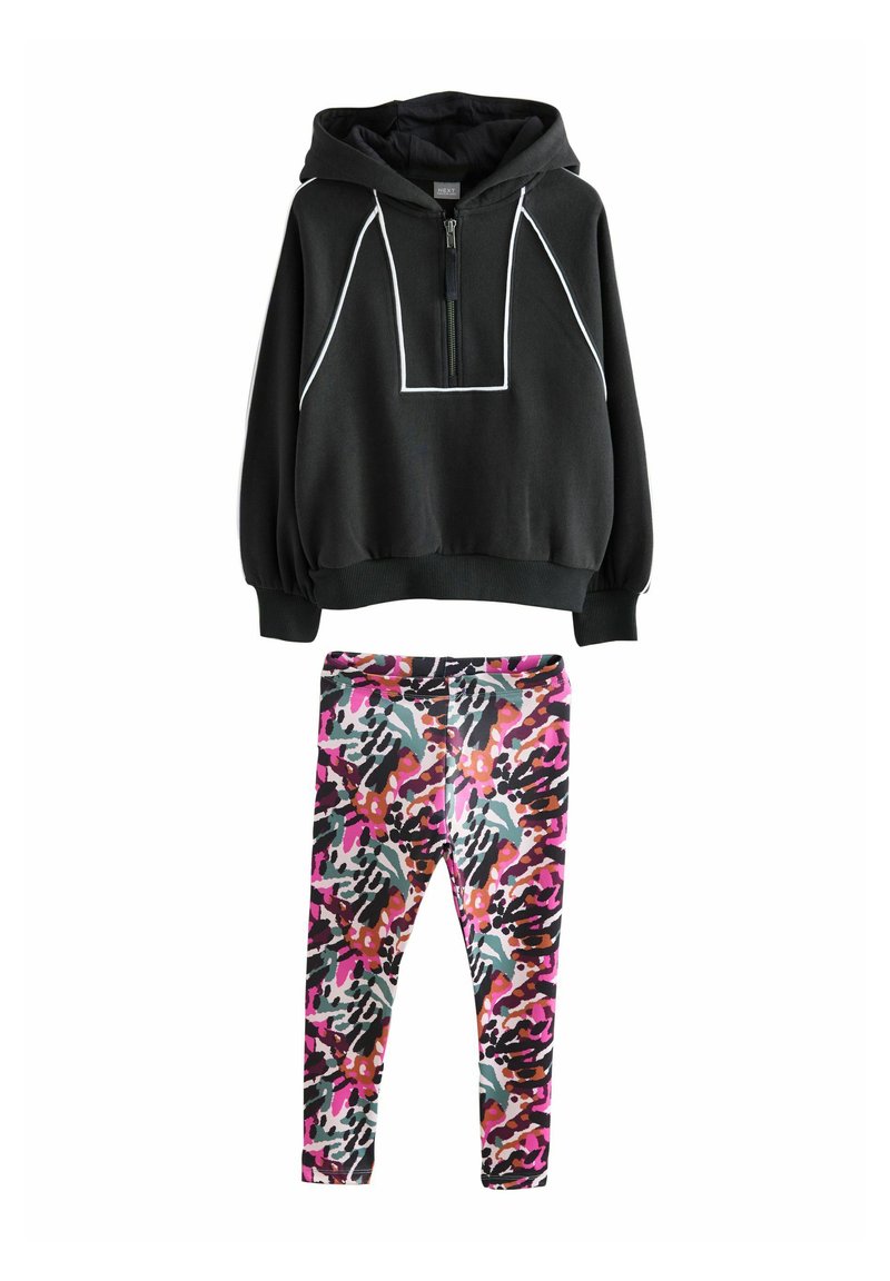 Svart zip-up hoodie med vita detaljer och känguruficka, kombinerad med färgglada, mönstrade tights i rosa, lila och svart. Material av bomullsblandning.