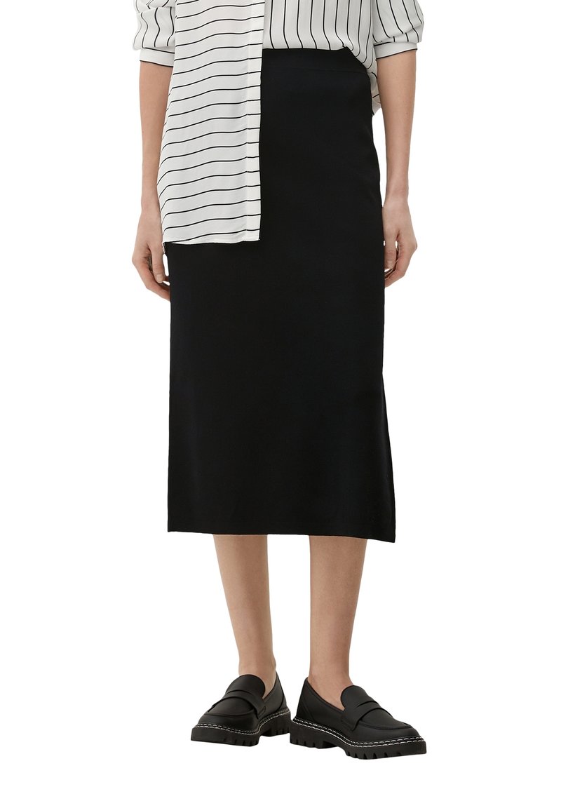 Schwarzer Midirock mit glatter Textur, kombiniert mit einer gestreiften weißen Bluse. Dazu passen klobige schwarze Loafers für einen eleganten Look.