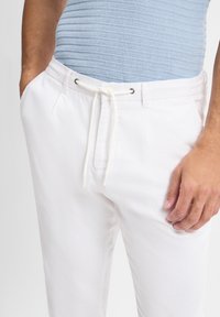 Witte broek met een gestructureerde afwerking, elastische tailleband en trekkoord. Voorzien van zijzakken en hardware-accenten in zilvertint.