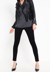 Svart lädermotorcykeljacka med silverdragkedjor, över en grå topp med högt krage, tillsammans med svarta skinnybyxor och svarta klackar.