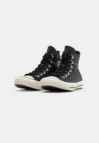 Sneaker alte nere in pelle testurizzata, con suole in gomma bianca, lacci neri e un accento di catena argentata sul lato.