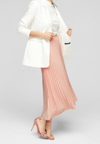 Blazer bianco, top bianco aderente e gonna plissettata rosa chiaro. Sandali con tacco a strappo rosa. Tessuto morbido, silhouette elegante.