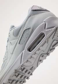 Gaiši pelēki Nike Air Max sneakeri, izgatavoti no acu un gumijas materiāliem, ar mīkstinātu apkakli, gaisa amortizāciju un strukturētu zoli.