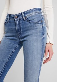 Ljusblå denim skinny jeans med hög midja, femfickorsdesign och subtil blekning. Har en kopparknapp och kontrasterande sömmar.