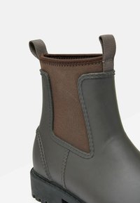 Szare gumowe kalosze za kostkę z brązową elastyczną wkładką, wzmocnionymi szwami i pętelką do zakładania. Gruba podeszwa z teksturowanym wzorem dla lepszej przyczepności.