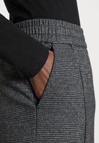 Pantaloni grigi a scacchi con un tessuto testurizzato e una vita elastica, dotati di una tasca laterale e una maglietta nera a maniche lunghe.