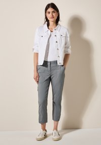 Giacca di jeans bianca, pantaloni grigi a vita alta e sneakers bianche. La giacca presenta chiusure a bottoni e due tasche frontali con una vestibilità classica.