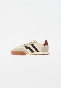 Beige Wildlederschuhe mit schwarzen Streifen, Gummisohle und karamellfarbener Fersenakzent. Verfügt über ein klassisches Low-Top-Design und Schnürverschluss.