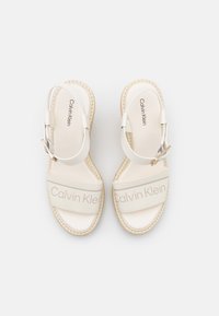 Białe sandały z wyściełaną wkładką, posiadające paski z logo "Calvin Klein" oraz detal w postaci klamry. Teksturowana podeszwa z przeszyciami.