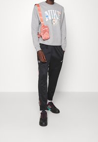 Grå sweatshirt med grafisk logotyp, svarta byxor med sidosträck samt svarta sneakers med färgglada detaljer och rosa snörning. Rosa crossbody-väska.