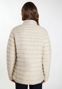 Giacca puffer beige con colletto alto, caratterizzata da un motivo trapuntato, texture liscia e tasche laterali. Vista posteriore, senza hardware visibile.