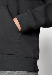 Mustansin sveitsi, jossa on kengurulompakko, ribbed-hihansuut ja helma, sileä pinta ja rento istuvuus.