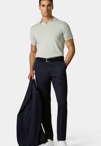 Světle šedý polo triko s krátkým rukávem, námořnické kalhoty, držící tmavý oblekový sako, doplněné bílými teniskami, se štíhlým střihem.