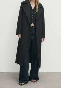 Mustat kaksiriviset takit, joilla on leveä kaulus, kerroksittain mustan liivin ja korkean vyötärön tummansinisten flare-farkkujen päällä, joissa on raikkaat helmat.