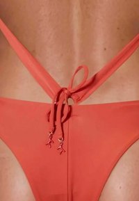 Rode bikini met een sleek ontwerp en een crisscross rug. Strikken met decoratieve rode bedels benadrukken de verstelbare pasvorm. Soepele textuur.