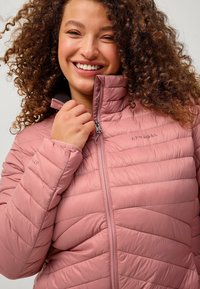 Lys rosa isoleret jakke med lynlås foran, høj krave og vandret quiltet mønster. Har et logo på brystet og glat stof.