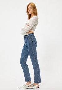 Jeans de mezclilla azul con corte recto, cintura alta y un ligero desvanecimiento. Combinados con una blusa corta de encaje blanca y zapatos planos blancos.